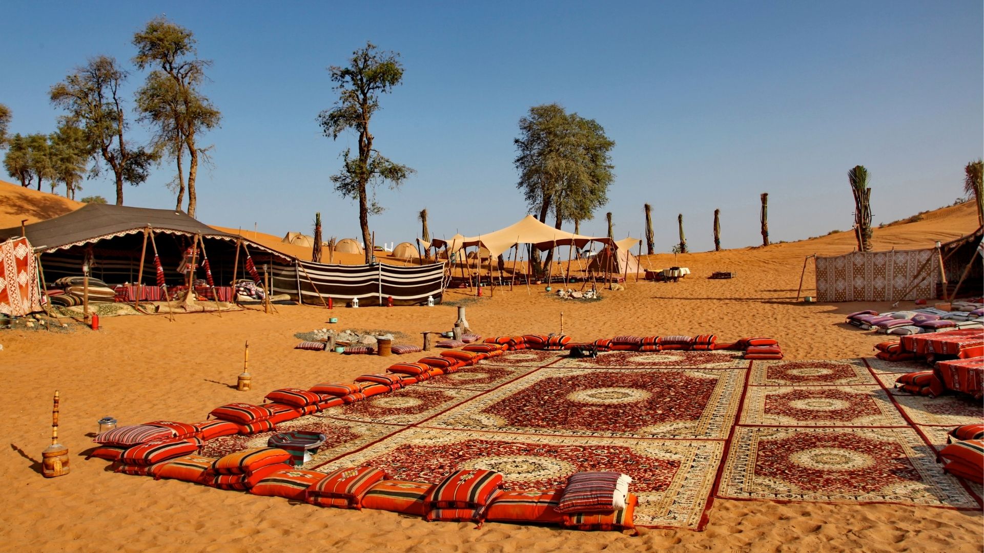 Marvel at the picturesque Bassata Village in the midst of a serene desert landscape, with the golden sands stretching out to the horizon and the clear blue sky overhead.