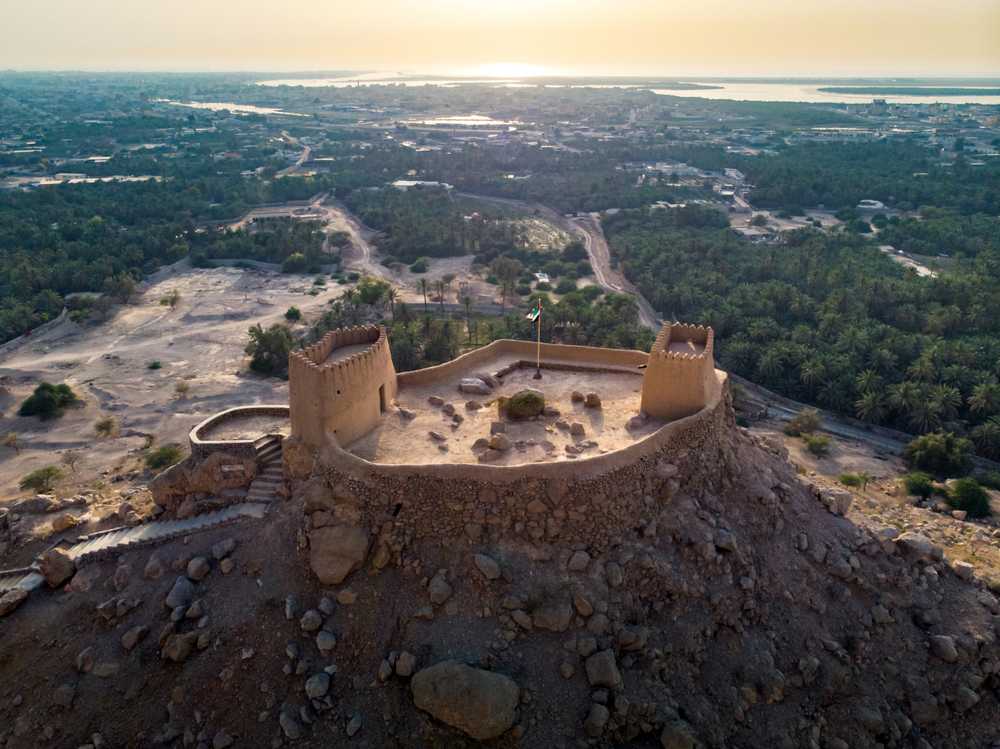 Aerial view of Dhayah Fort, an ancient fort located in Ras Al Khaimah, United Arab Emirates with a panoramic view of the surrounding mountains and coastline.