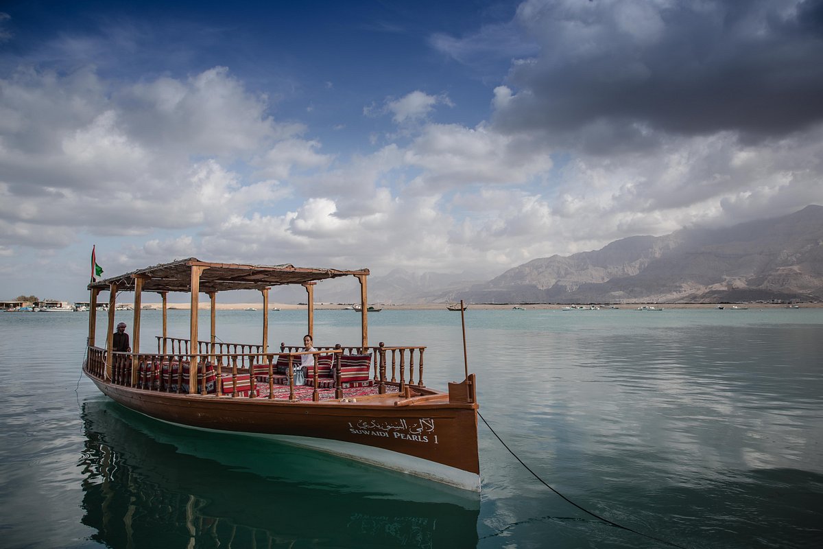 Image of a person on a traditional wooden dhow boat ride at Suwaidi Pearls, enjoying the picturesque view of mountains in the background
