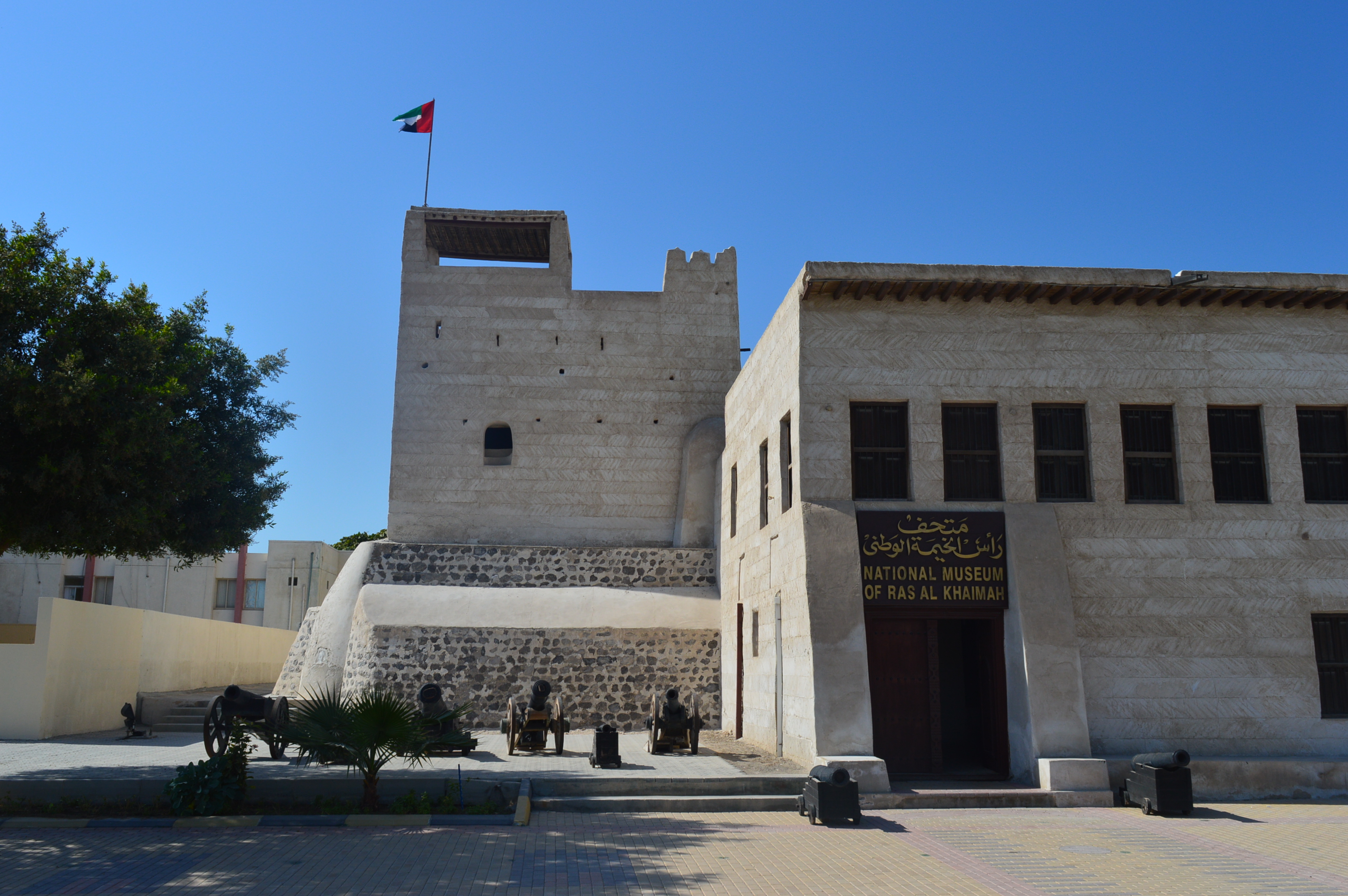 Picture of the Ras Al Khaimah National Museum's front: a traditional Emirati building with a courtyard, arched doorways, and white stone walls.