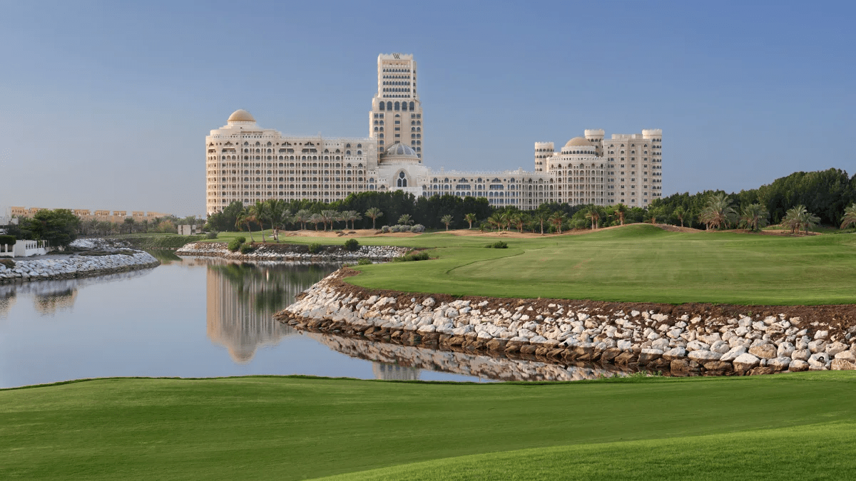 Exterior view of the Waldorf Astoria in Ras Al Khaimah, featuring lush greenery and a golf course in the foreground, with the hotel building in the background.